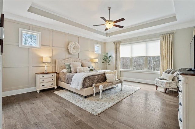 bedroom featuring hardwood / wood-style flooring, ornamental molding, ceiling fan, and a tray ceiling