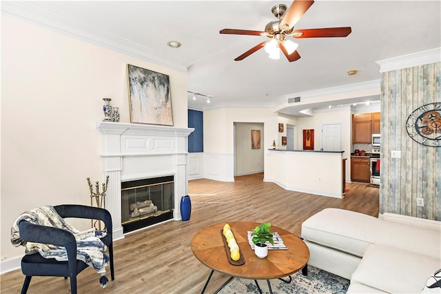 living area featuring ornamental molding, a glass covered fireplace, and light wood-style flooring