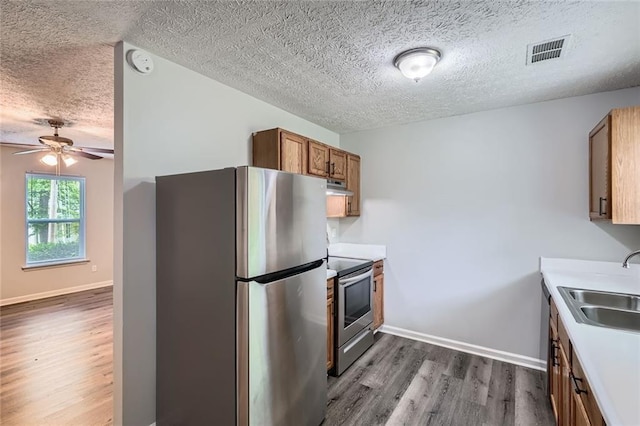 kitchen with brown cabinets, appliances with stainless steel finishes, a textured ceiling, dark wood-type flooring, and visible vents