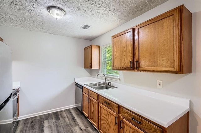 kitchen with brown cabinets, appliances with stainless steel finishes, a sink, dark wood-type flooring, and visible vents