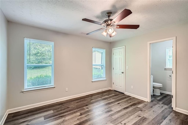unfurnished bedroom featuring a textured ceiling, multiple windows, baseboards, and wood finished floors
