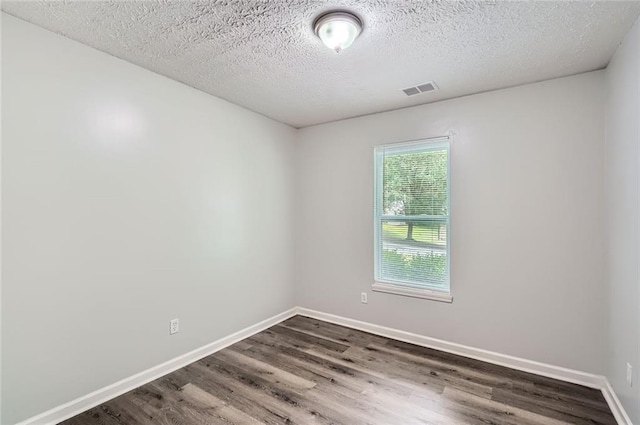 spare room featuring a textured ceiling, baseboards, visible vents, and dark wood-type flooring