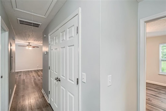 hallway with visible vents, attic access, a textured ceiling, and wood finished floors