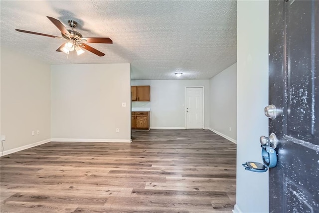 interior space featuring baseboards, a ceiling fan, a textured ceiling, and wood finished floors