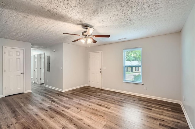 spare room with ceiling fan, baseboards, wood finished floors, visible vents, and electric panel