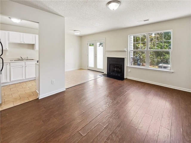 unfurnished living room with sink, light hardwood / wood-style floors, french doors, and a textured ceiling