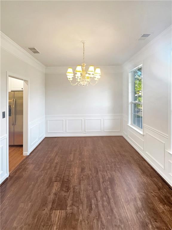 unfurnished dining area featuring crown molding, an inviting chandelier, and dark wood-type flooring