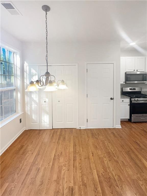 unfurnished dining area featuring light wood-type flooring, a healthy amount of sunlight, and a notable chandelier