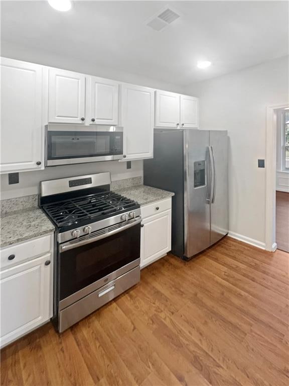 kitchen featuring light stone counters, stainless steel appliances, white cabinetry, and light hardwood / wood-style flooring