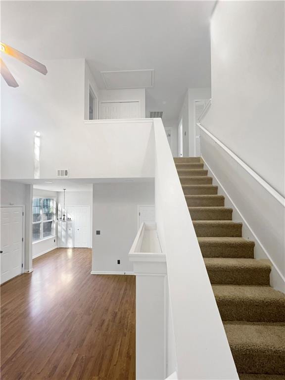 staircase featuring ceiling fan with notable chandelier, a high ceiling, and hardwood / wood-style flooring