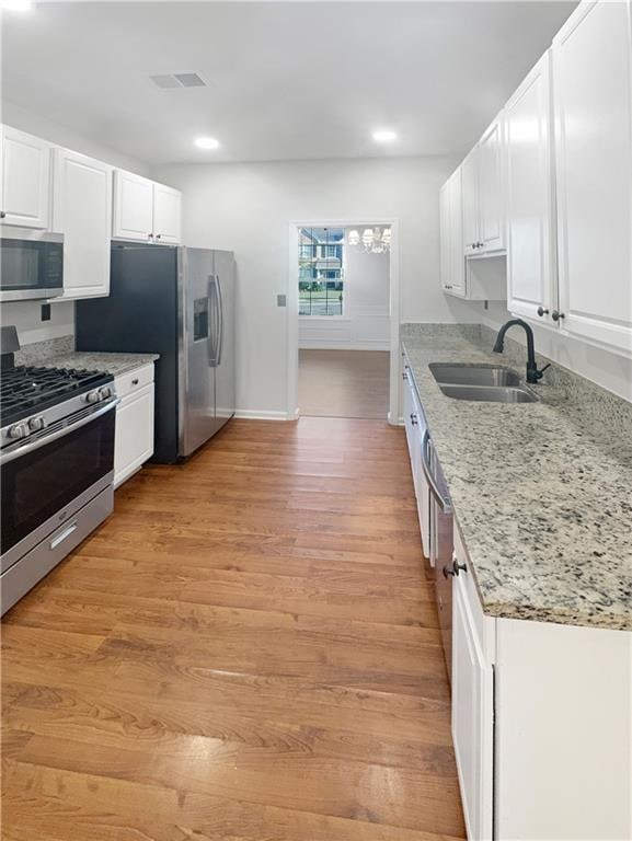 kitchen featuring appliances with stainless steel finishes, white cabinetry, light stone counters, light wood-type flooring, and sink