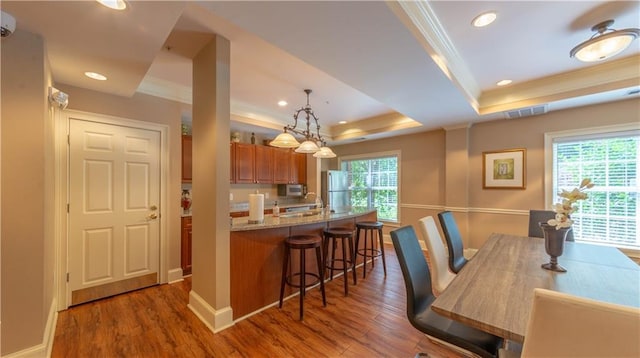 3275 Lenox Rd NE Unit 413, Atlanta, GA 30324 - kitchen featuring crown molding, a raised ceiling, brown cabinets, a kitchen bar, and wood finished floors