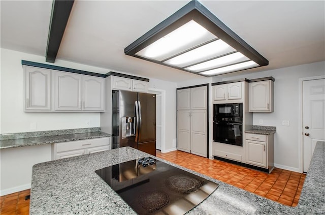 kitchen with black appliances, light stone countertops, white cabinetry, and baseboards