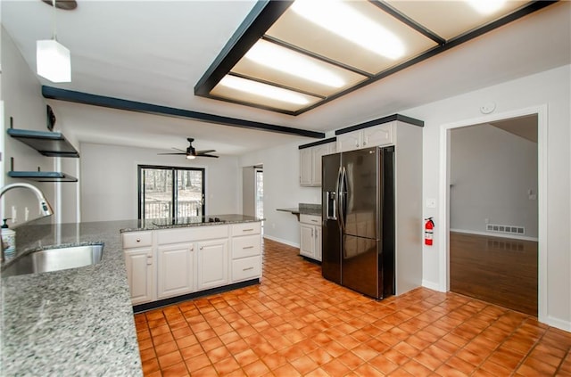 kitchen featuring light stone counters, a sink, white cabinets, hanging light fixtures, and black appliances