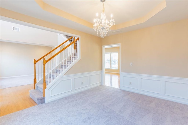 empty room featuring visible vents, a raised ceiling, stairway, an inviting chandelier, and carpet