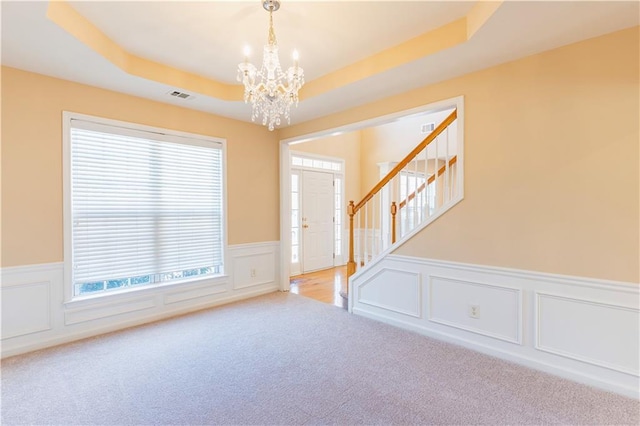 empty room featuring visible vents, stairway, carpet, a tray ceiling, and a chandelier