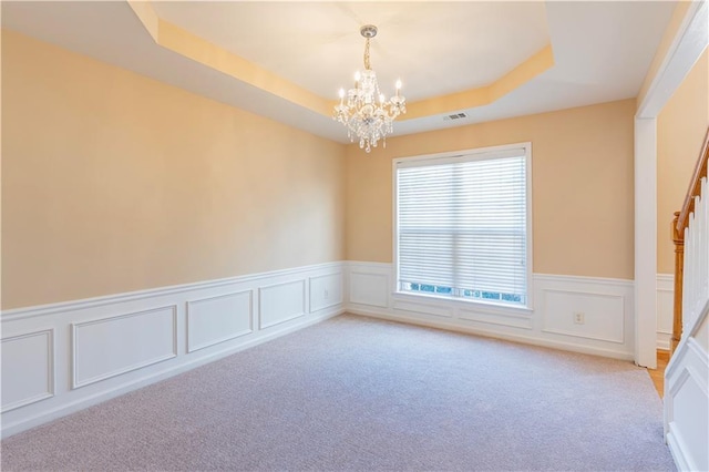 empty room with a notable chandelier, light carpet, a wainscoted wall, visible vents, and a raised ceiling