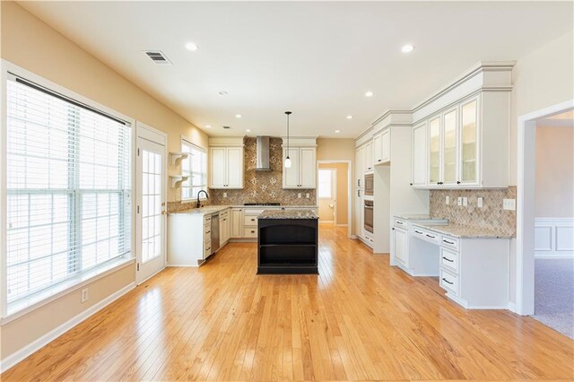 kitchen with visible vents, wall chimney exhaust hood, light wood-style flooring, stainless steel appliances, and a sink