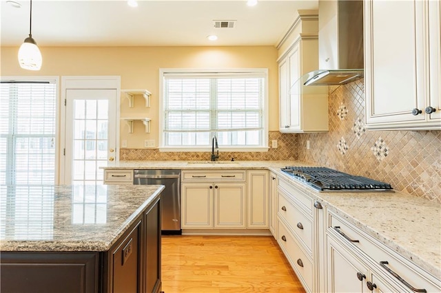 kitchen featuring stainless steel appliances, a sink, visible vents, wall chimney range hood, and tasteful backsplash