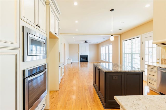 kitchen featuring light wood-type flooring, light stone countertops, a fireplace, and stainless steel appliances