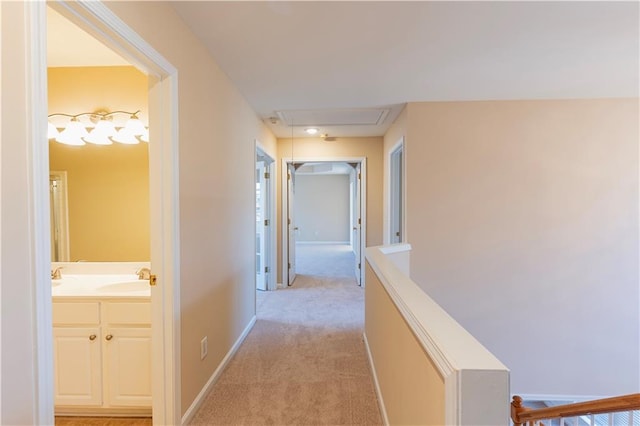 corridor with light carpet, attic access, baseboards, an upstairs landing, and a sink