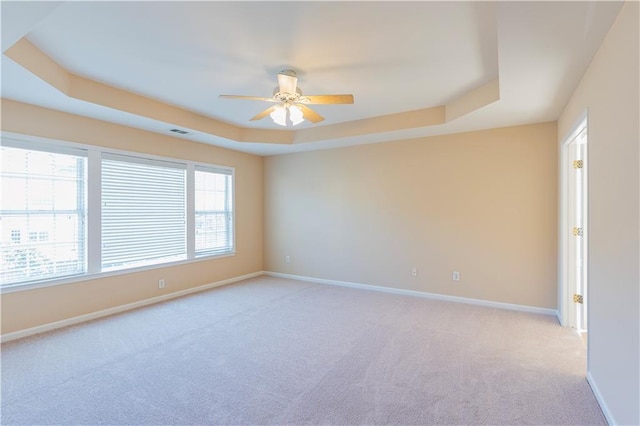 empty room featuring light carpet, a ceiling fan, visible vents, baseboards, and a tray ceiling