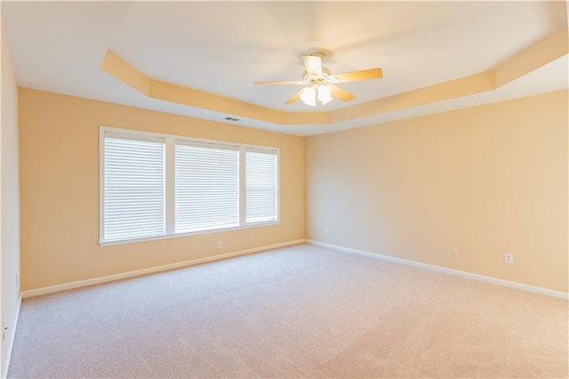 unfurnished room featuring a raised ceiling, visible vents, light carpet, ceiling fan, and baseboards