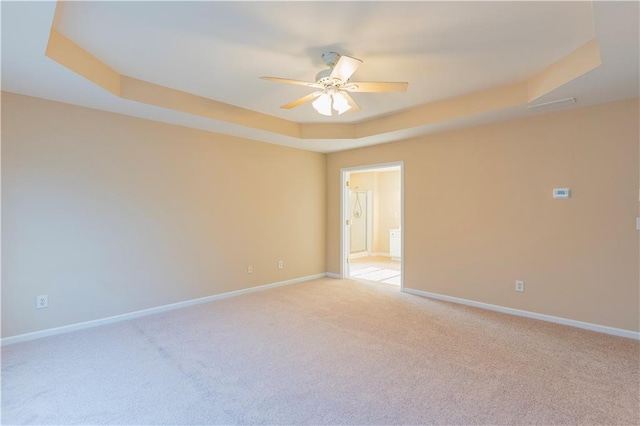 empty room with light carpet, ceiling fan, a raised ceiling, and baseboards