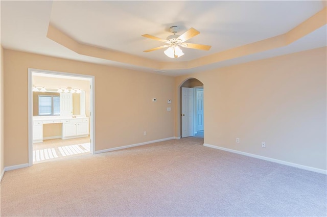 unfurnished room featuring light carpet, baseboards, arched walkways, and a raised ceiling