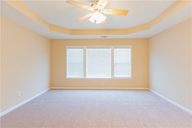 spare room featuring light carpet, a tray ceiling, visible vents, and baseboards