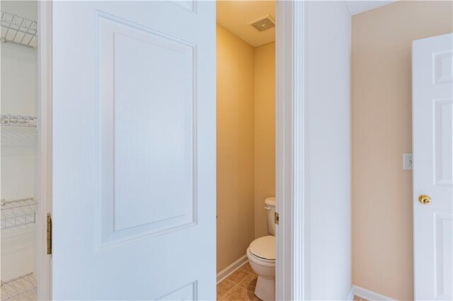 bathroom with a walk in closet, visible vents, toilet, baseboards, and tile patterned floors