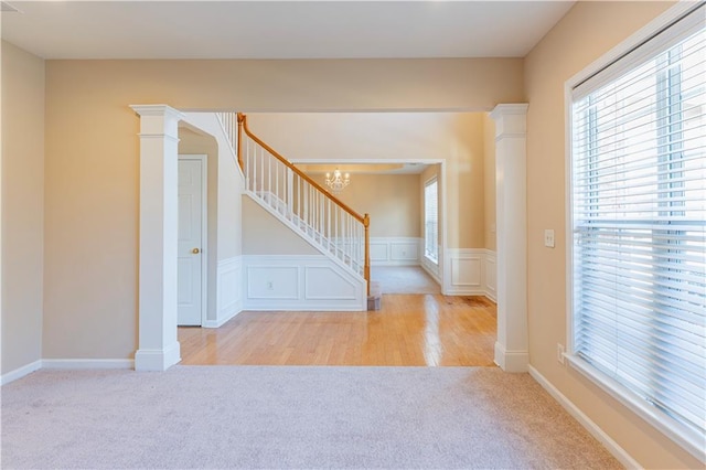 carpeted empty room featuring a wainscoted wall, decorative columns, a decorative wall, stairway, and a chandelier