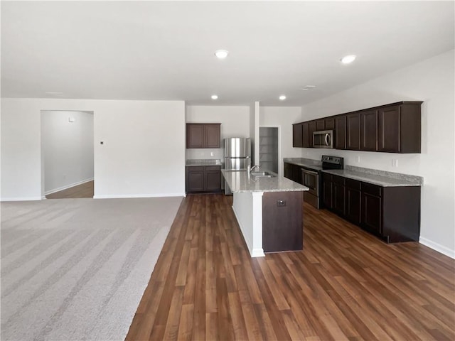 kitchen with an island with sink, dark wood-style floors, appliances with stainless steel finishes, and dark brown cabinets