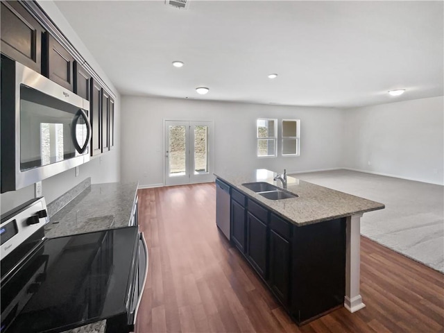 kitchen with light stone counters, appliances with stainless steel finishes, dark wood-type flooring, open floor plan, and a sink