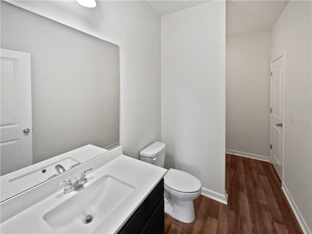 half bathroom with toilet, baseboards, wood finished floors, and vanity