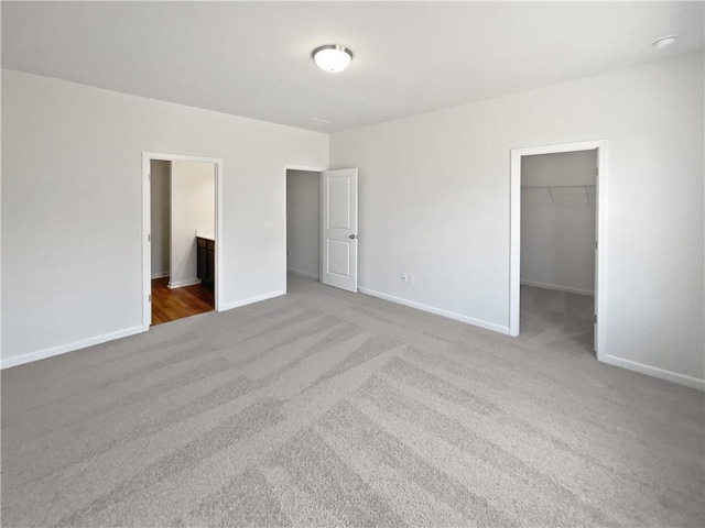 unfurnished bedroom with baseboards, ensuite bathroom, carpet, a walk in closet, and a closet