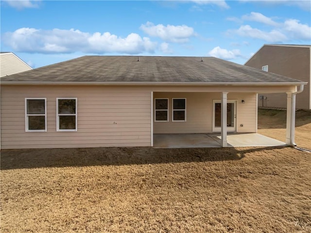 rear view of house with a shingled roof, a patio, and a lawn