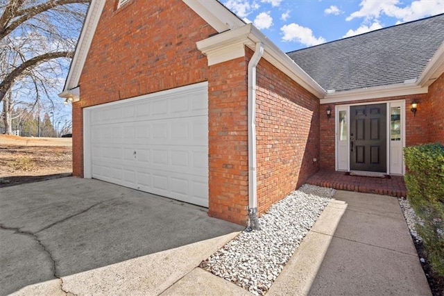 property entrance with a garage, a shingled roof, concrete driveway, and brick siding