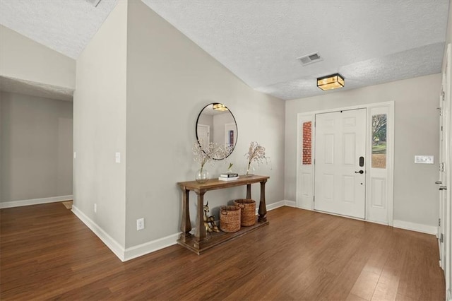 entrance foyer with a textured ceiling, dark wood-style flooring, visible vents, and baseboards