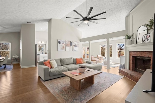 living area with dark wood-type flooring, a fireplace, a textured ceiling, and ornate columns