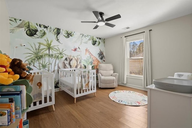 bedroom with ceiling fan, a crib, wood finished floors, and visible vents