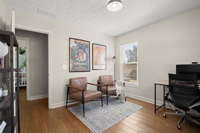 office space featuring visible vents, a textured ceiling, baseboards, and wood finished floors