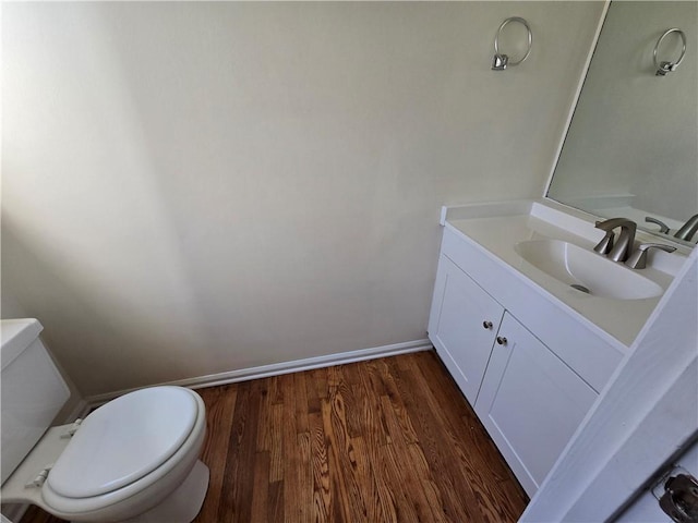 half bath featuring baseboards, vanity, toilet, and wood finished floors