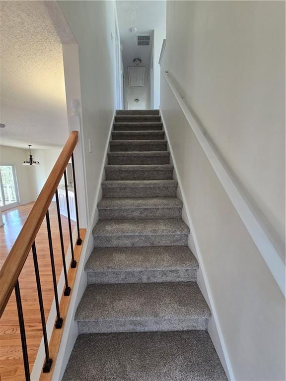 stairway with visible vents, a textured ceiling, baseboards, and wood finished floors