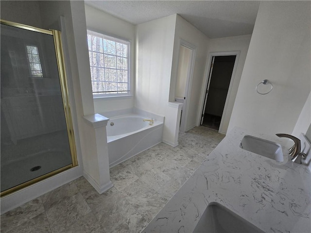 full bath featuring baseboards, a garden tub, a textured ceiling, a shower stall, and a sink