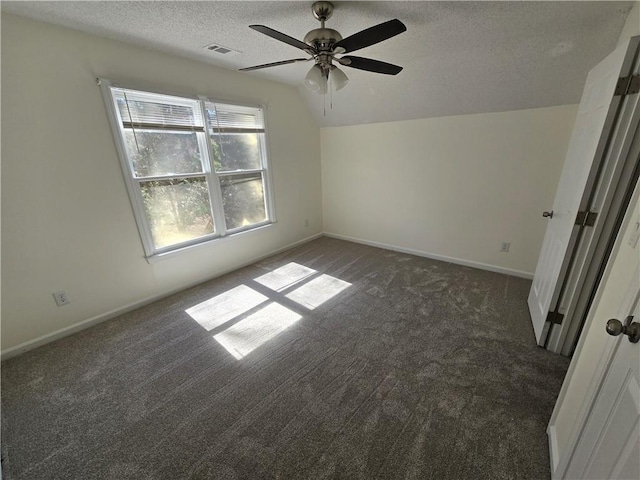 empty room with dark colored carpet, visible vents, vaulted ceiling, a textured ceiling, and baseboards