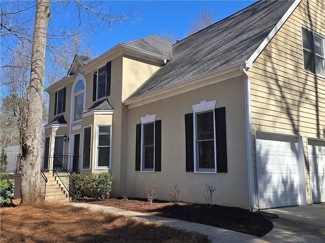 view of side of property featuring a garage, a shingled roof, and stucco siding