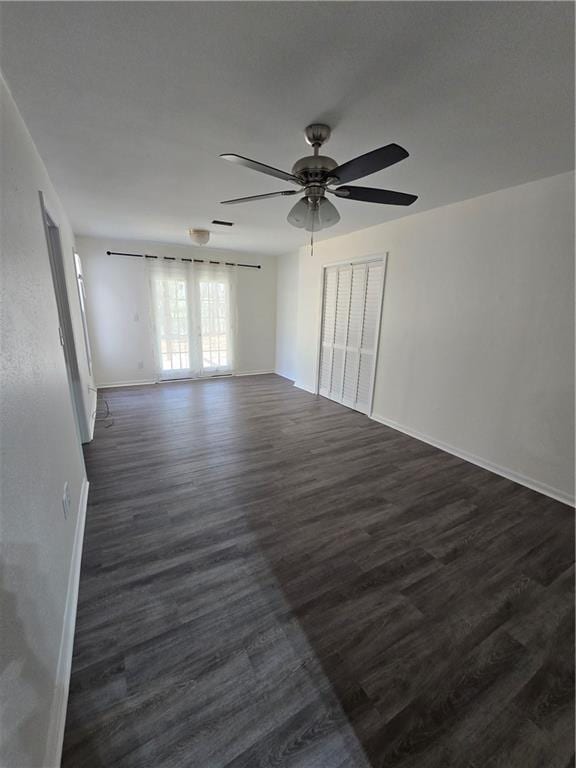 spare room featuring ceiling fan, baseboards, and dark wood finished floors