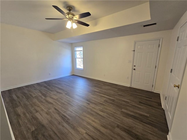 empty room featuring a ceiling fan, visible vents, dark wood finished floors, and baseboards