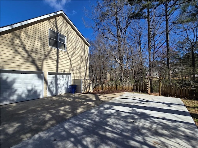 view of side of home with a garage, concrete driveway, and fence